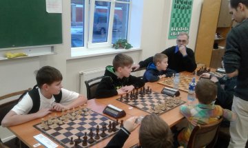 Gaidot kārtējo kārtu. No kreisās: Emīls Grīnerts, Ingars Blumbergs, Ernests Brikainis un ... skolotājs Alnis Auziņš, kas, biedēdams mazo pretinieci, apsēdies pie meiteņu galdiņa.